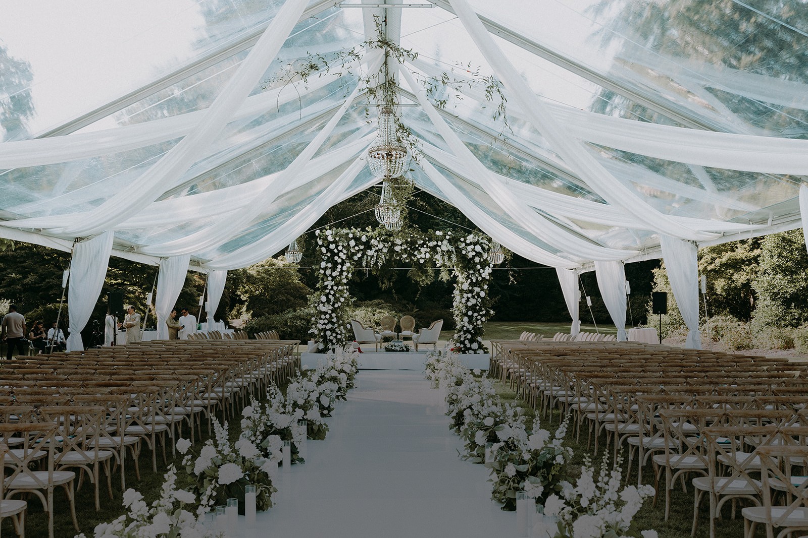 Bright clear-span tent interior with chandelier and a dark floral arch at a wedding