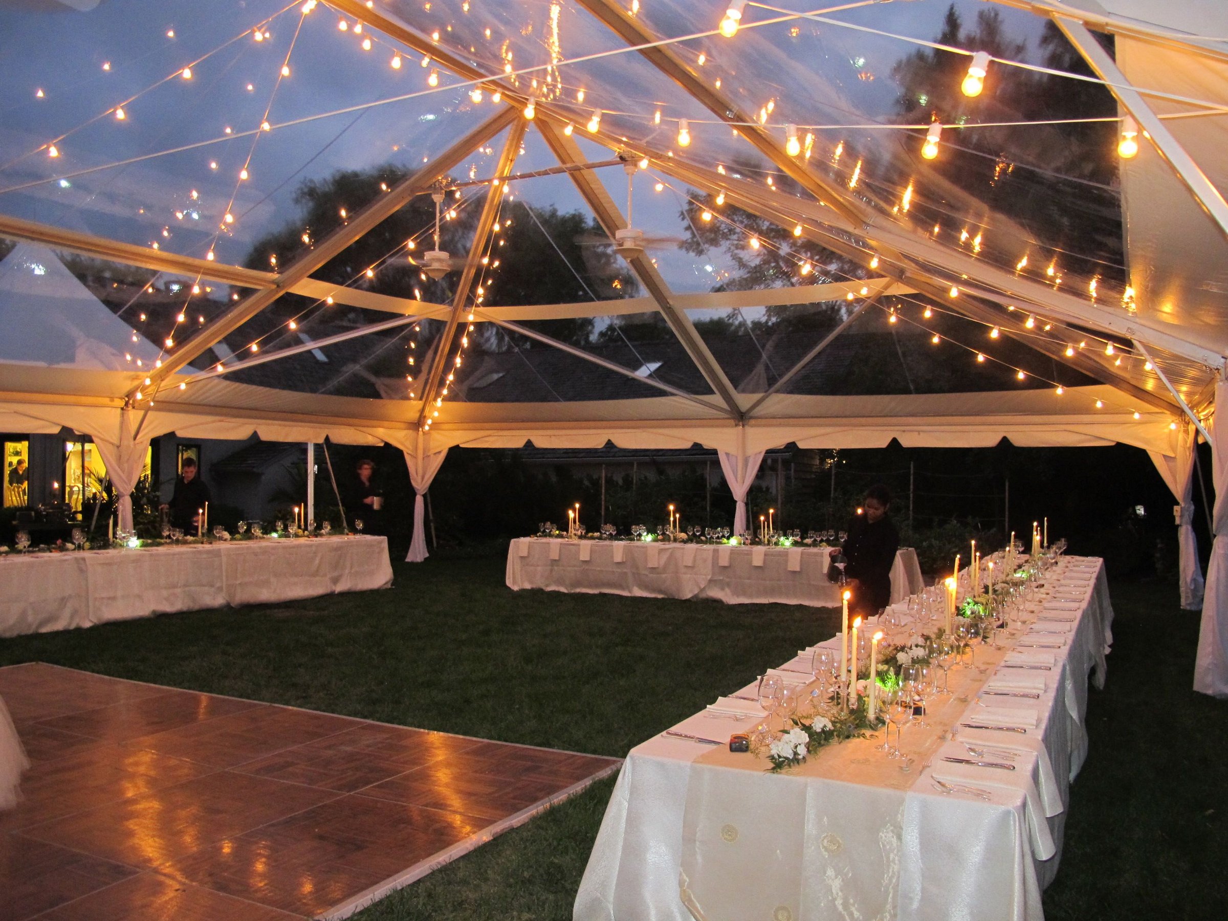 Clearspan tent wedding reception at dusk with string lights and tables set for dinner